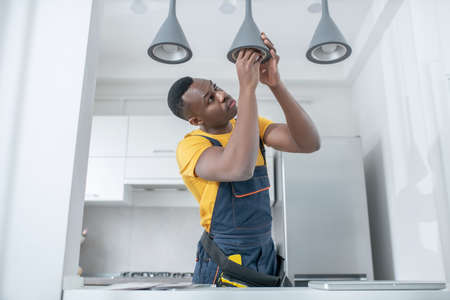 Electrician. Dark-skinned service man in yellow tshirt repairing electricity lampsの写真素材