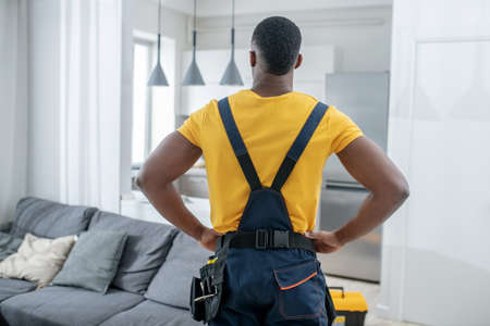 In the kitchen. Dark-skinned service man in yellow tshirt standing in the kitchen