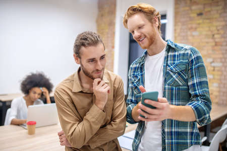 Interesting stuff. Two male colleagues discussing something while looking at the phone abd looking enjoyedの写真素材