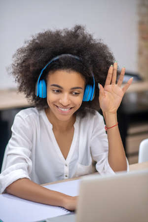 Audio call. Dark-skinned pretty girl in earphones sitting at the table