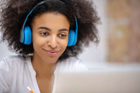 Audio call. Dark-skinned pretty girl in earphones sitting at the table