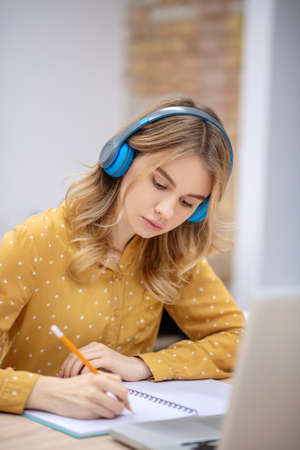 Listening to the lecture. Blonde pretty girl in earphones sitting at the table and listening...