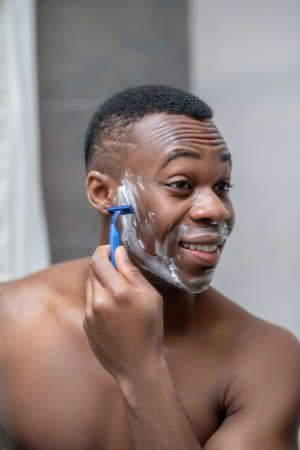 African american young handsome man shaving iand looking positiveの写真素材