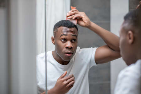 African american guy in white tshirt doing his hair in the bathroomの写真素材