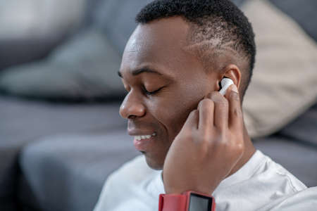 African american guy in white clothes wearing wireless earphone