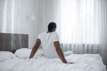 African american man sitting on bed and stretchingの写真素材