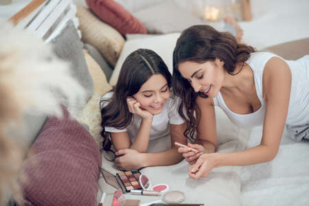 Woman trying cosmetic pencil and interested girlの写真素材