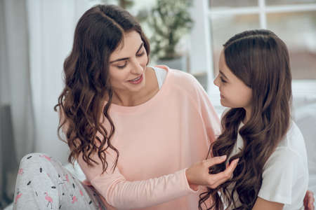 Smiling mom touching daughters long wavy hairの写真素材
