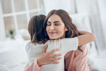 Happy mom with closed eyes hugging daughter tightlyの写真素材
