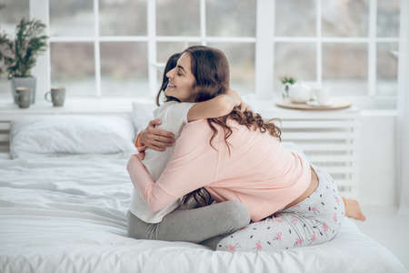 Mom and daughter hugging on bed in morningの写真素材