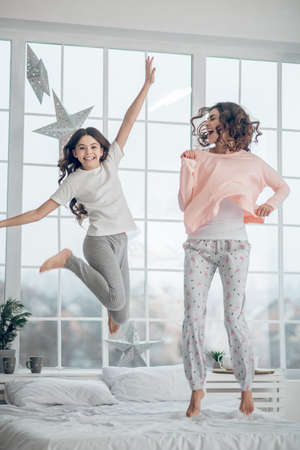 Woman with teenage girl jumping on bed at homeの写真素材