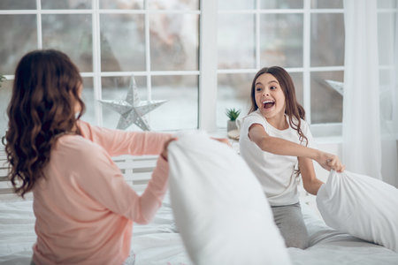 Daughter and mom playing beating pillowsの写真素材