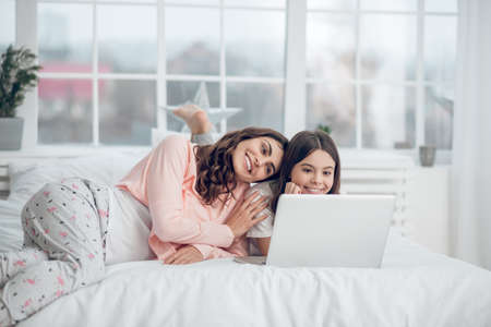 Girl and woman in pajamas near laptop in bedの写真素材