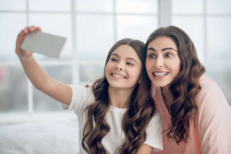 Long haired adorable mom and daughter taking selfieの写真素材