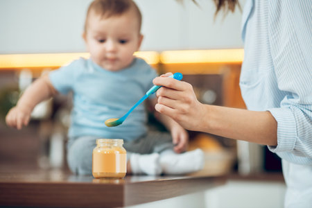 Female hand with spoon near jar of baby foodの写真素材