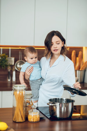 Mom with child looking into saucepan on stoveの写真素材