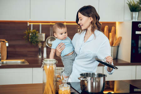 Woman with child opening saucepan on stoveの写真素材