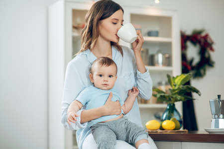 Woman with baby and cup near her mouthの写真素材