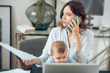 Woman with smartphone and documents sitting with childの写真素材