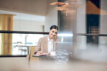 Young businesswoman in beige jacket sitting in the office in front of the laptopの写真素材