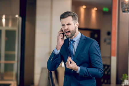 Businessman in a blue suit talking on the phone and looking agressiveの写真素材