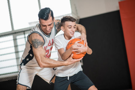 Dark-haired man playing basketball with a boy