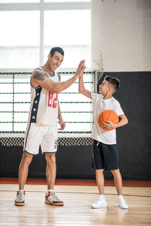 Coach in white sportswear teaching the boy playing basketballの写真素材