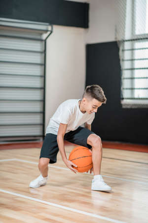 A boy playing basketball in the gym and looking involvedの写真素材