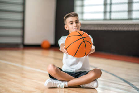 A dark-haired boy sitting on the floor and holding a ball in handsの写真素材