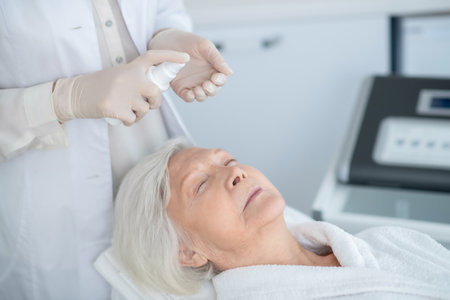 Cosmetologist working with a mature customer and preparing face cream for applyingの写真素材