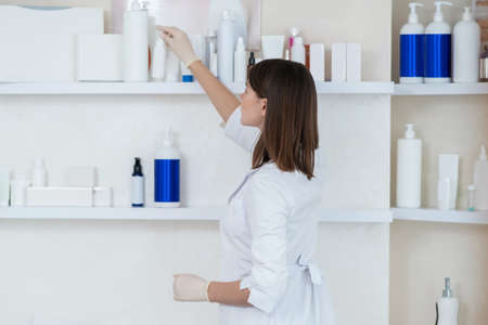 Cosmetologist in a white coat taking beauty products from the shelfの写真素材