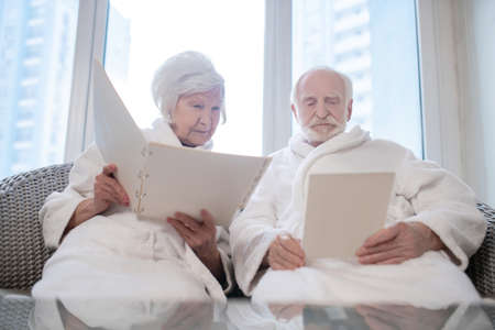 Senior couple in white robes choosing procedures in a spa centerの写真素材