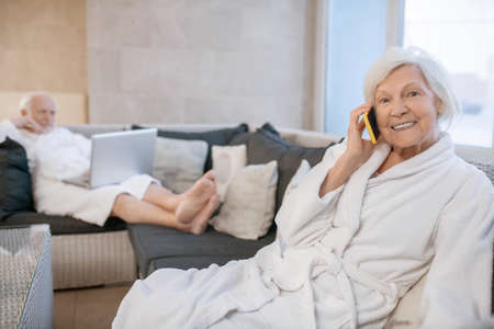 Gray-haired smiling woman looking pleased and talking on the phoneの写真素材