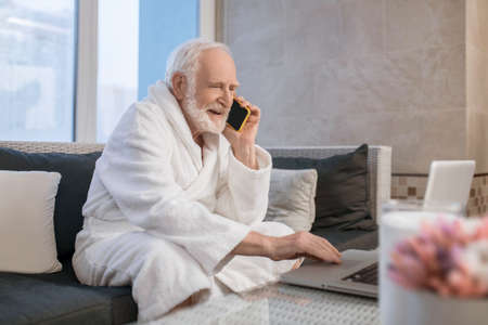 Gray-haired bearded man in white robe talking on the phone and looking busyの写真素材