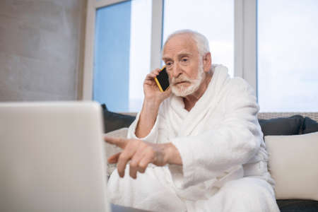 Gray-haired bearded man in white robe talking on the phone and looking busy