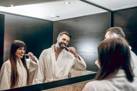 Man and woman in bath robes brushing teeth togetherの写真素材
