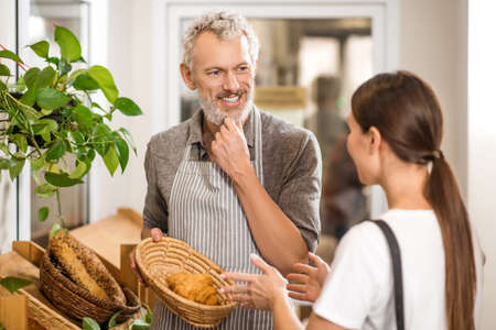 Man in apron showing croissant to customer