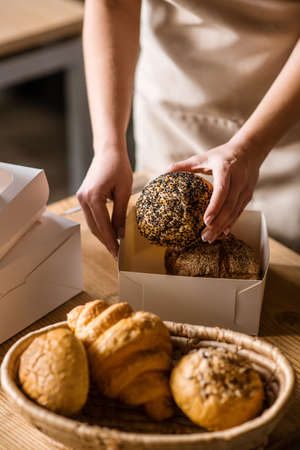 Caring female hand with bread bun over packagingの写真素材