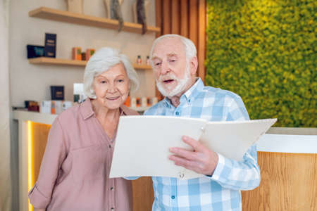 Gray-haired couple looking trhough the price list in spa center and looking interestedの写真素材