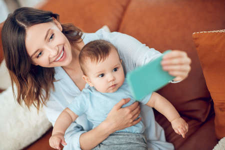 Cheerful woman with child taking selfie on smartphone