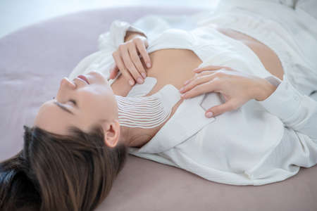 Young woman in white lying with tapes on her neck and looking relaxed