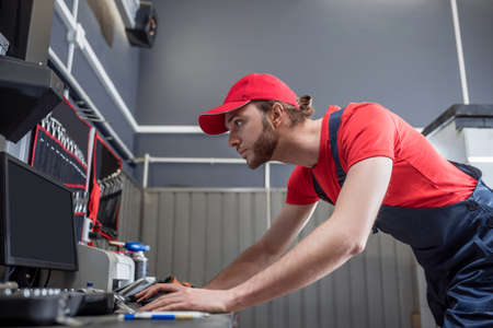 Man in overalls standing looking at computer monitorの写真素材