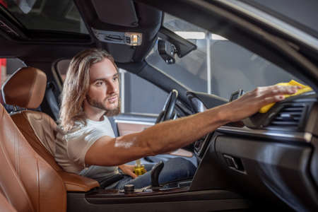 Attractive man wiping surfaces in car interiorの写真素材