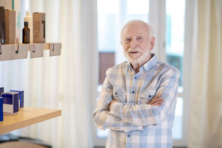 Gray-haired man in a plaid shirt in choosing beauty products in a beauty salonの写真素材