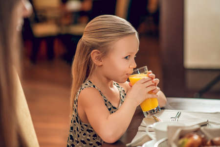 Cute girl sitting at the table and drinking orange juiceの写真素材