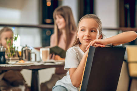 Sweet girl sitting at the table in the restaurant with familyの写真素材