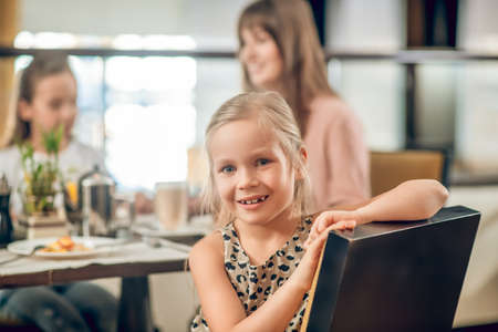 Sweet girl sitting at the table in the restaurant with familyの写真素材
