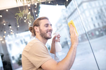 Satisfied man wiping glass surface in cafeの写真素材