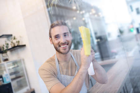 Happy young man wiping glass while in cafeの写真素材