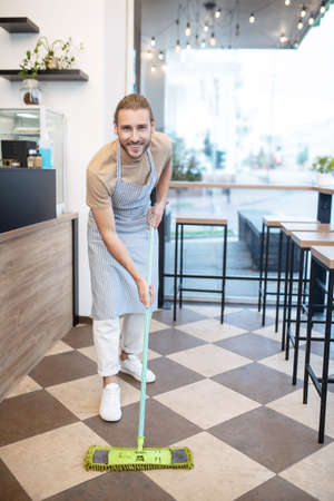 Smiling man cleaning floor in his cafeの写真素材